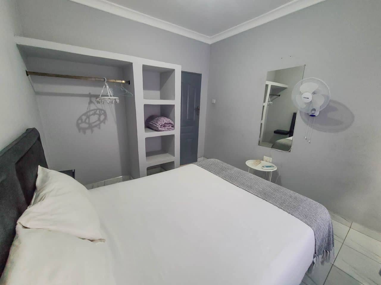 A bedroom with a bed, a wardrobe, a mirror, and a small table.