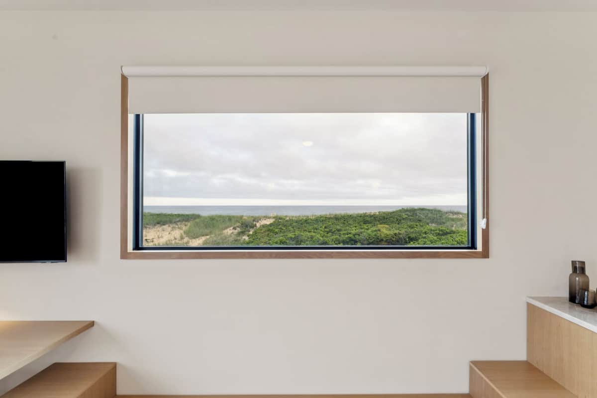 Une pièce dotée d’une grande fenêtre donnant sur un paysage naturel, d’un téléviseur à écran plat fixé au mur et d’un banc en bois.