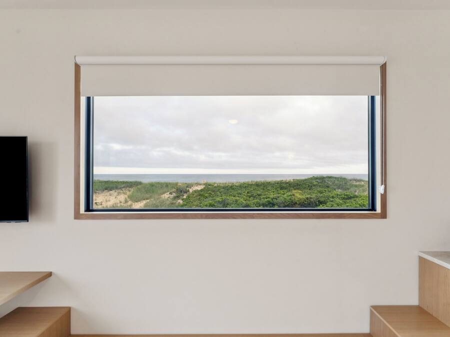Une pièce dotée d’une grande fenêtre donnant sur un paysage naturel, d’un téléviseur à écran plat fixé au mur et d’un banc en bois.