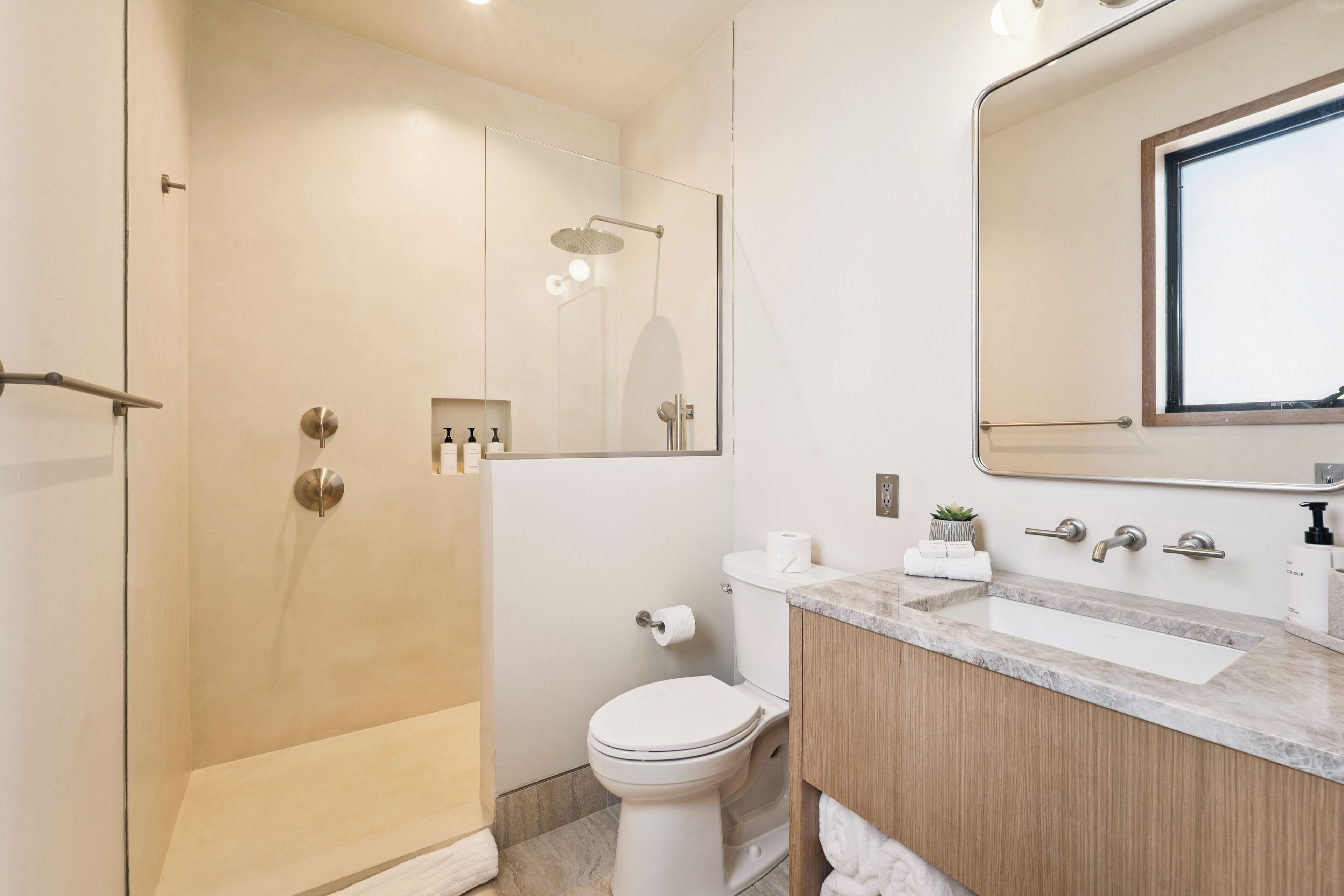 A modern bathroom with a glass-enclosed shower, a toilet, and a vanity with a mirror.