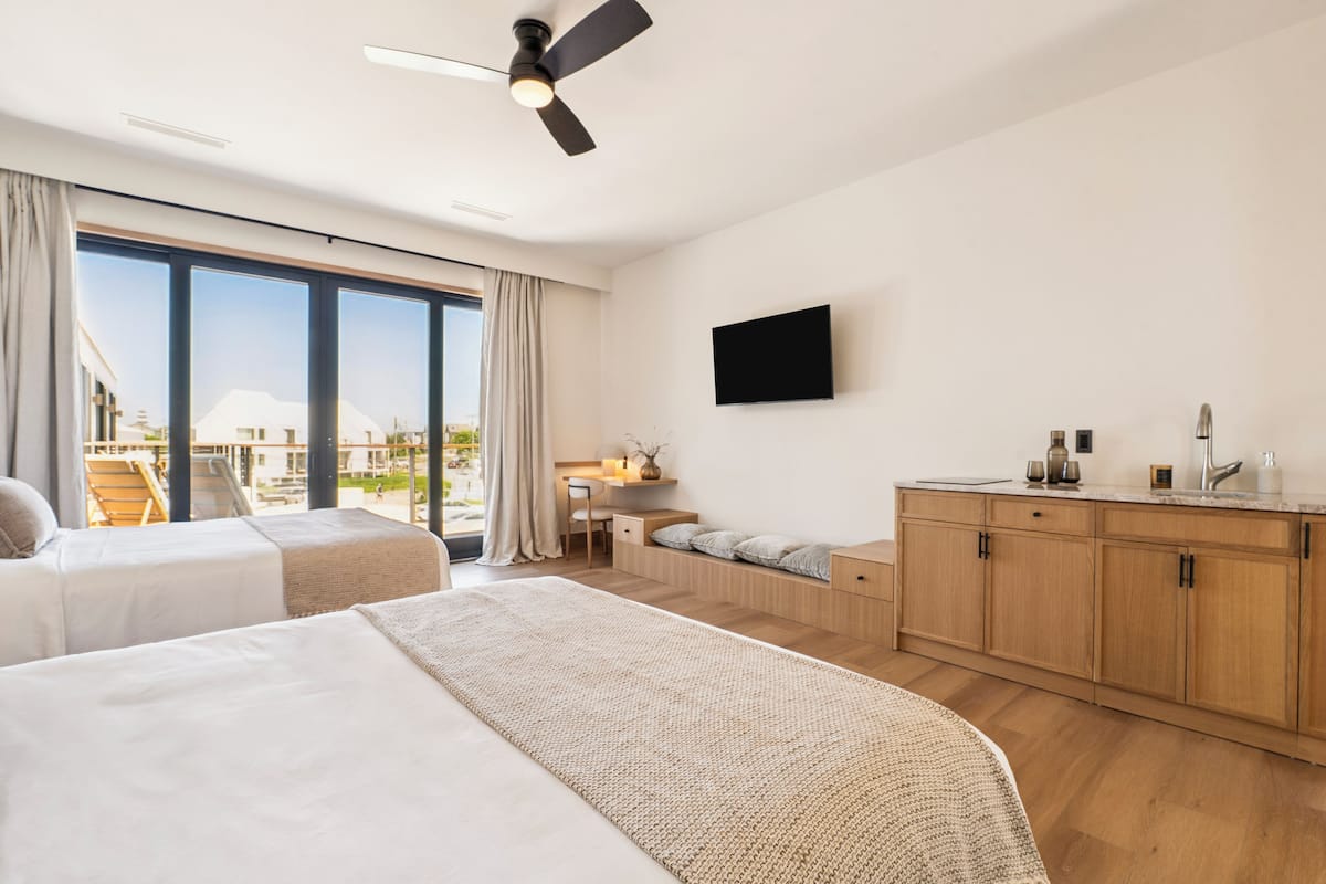 Une chambre d’hôtel moderne dotée de deux lits, d’un bureau, d’une télévision à écran plat et d’un balcon offrant une vue sur la ville.