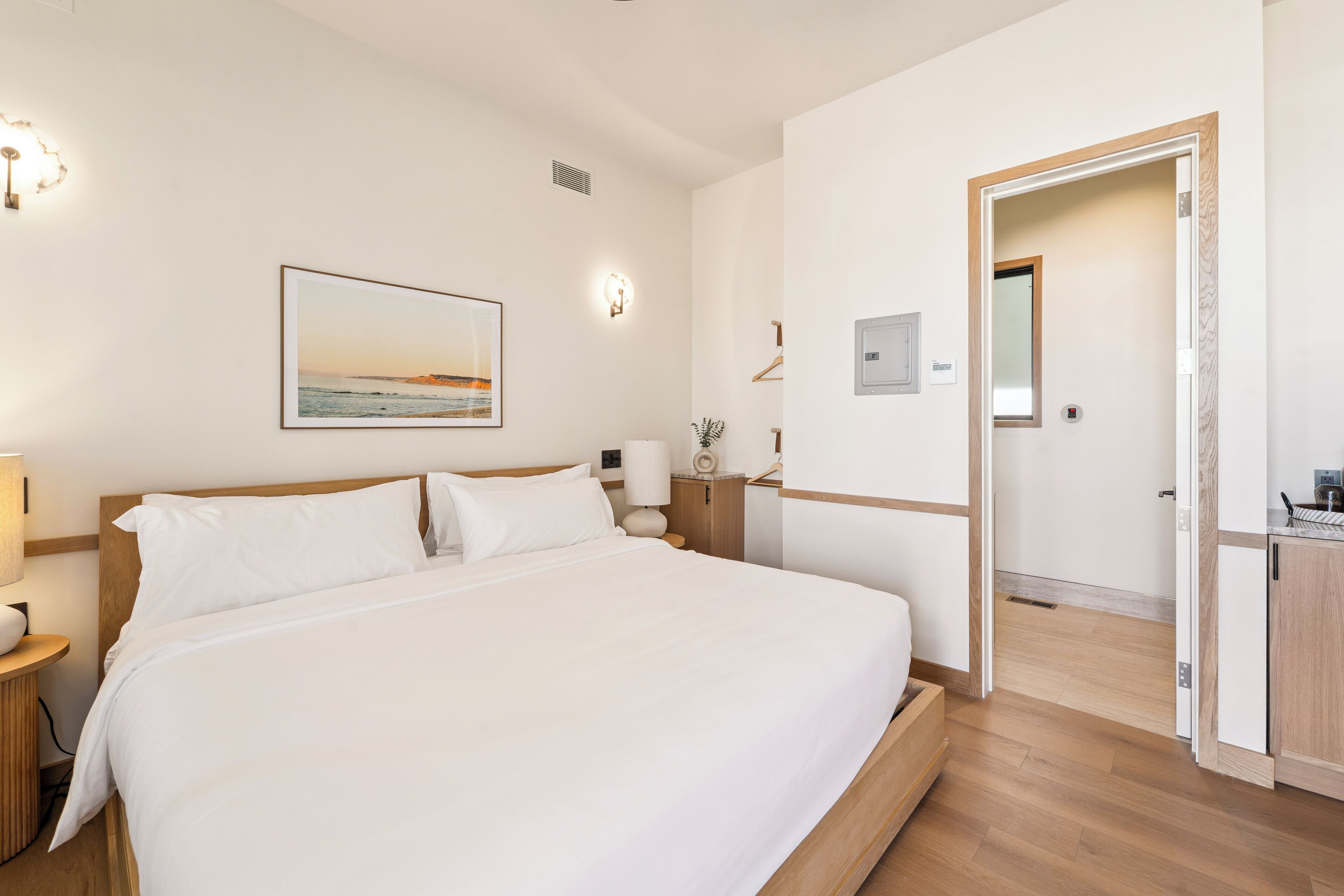A neatly arranged bedroom with a large bed, bedside lamps, a framed picture on the wall, and a wooden cabinet.