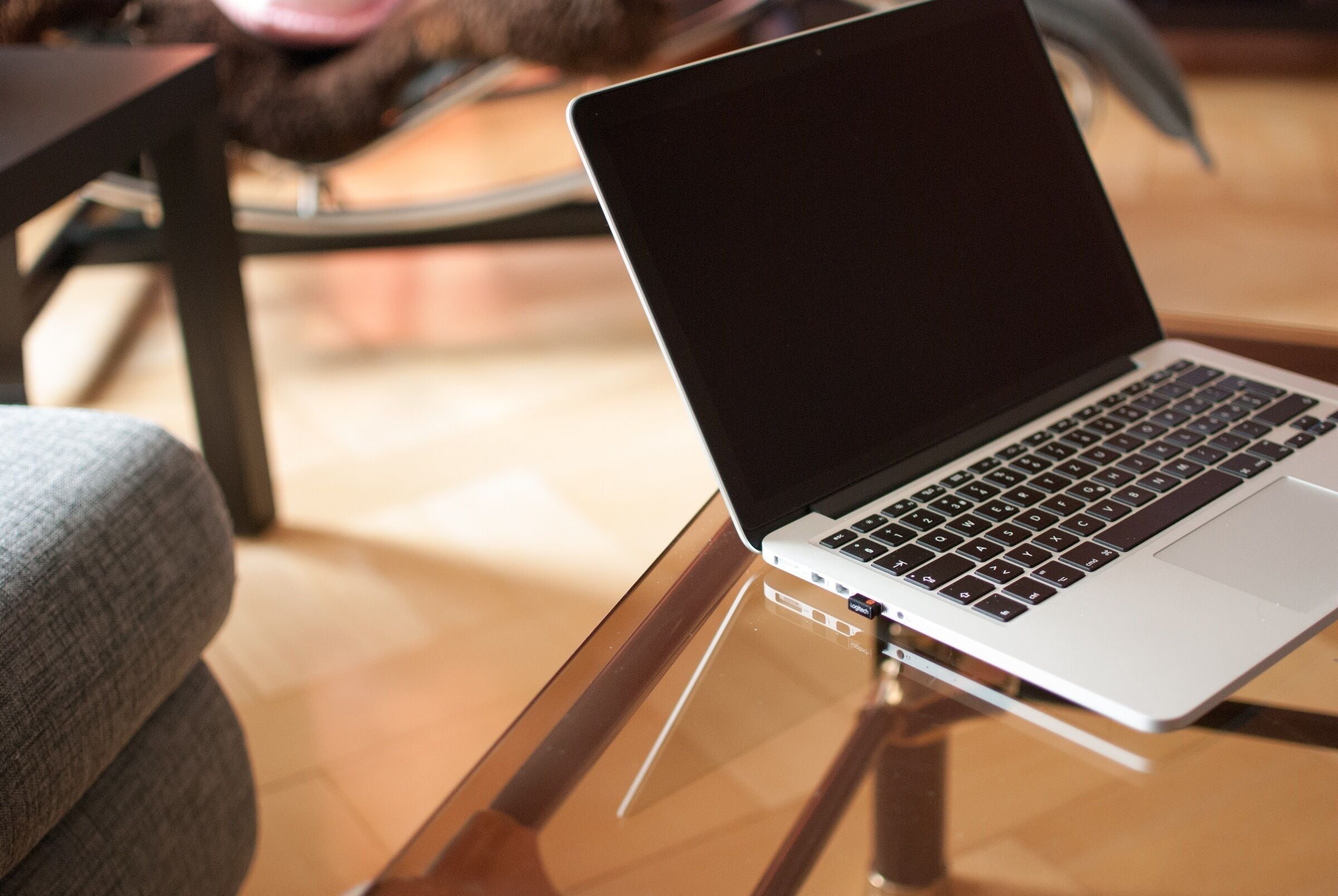 Ein Laptop auf einer Glastischplatte, im Hintergrund ein Stuhl.