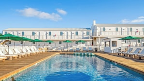 A swimming pool with lounge chairs and umbrellas, surrounded by a white building with multiple windows. - Offshore Montauk (Montauk)