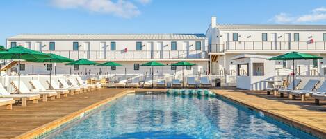 A swimming pool with lounge chairs and umbrellas, surrounded by a white building with multiple windows.