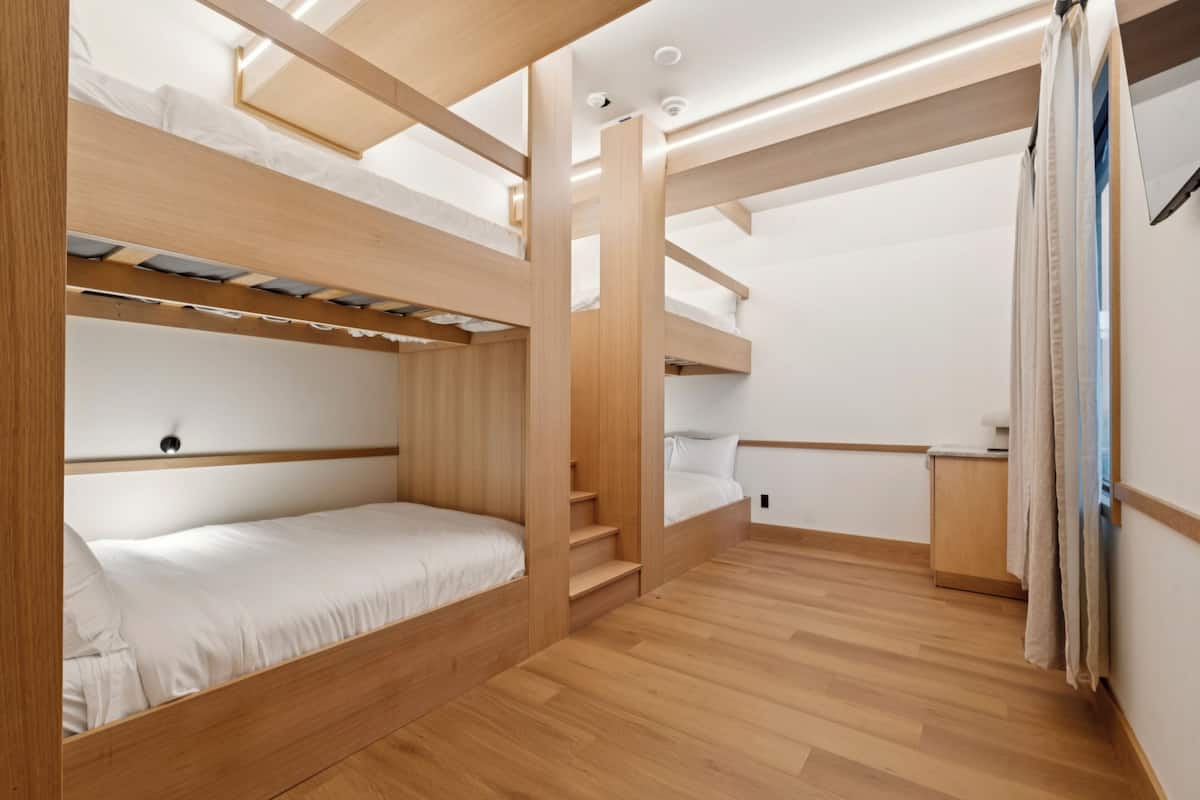 Une chambre avec des lits superposés, un plancher en bois et un éclairage intégré.