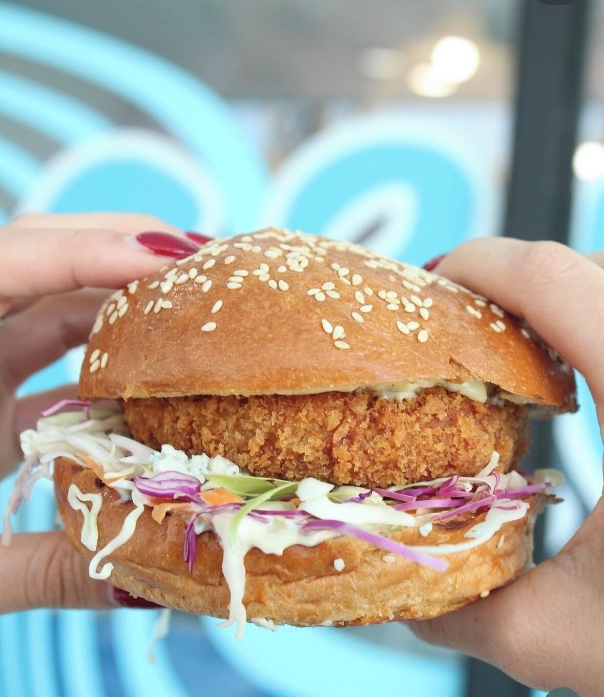 A sandwich with sesame seeds on the bun, a crispy chicken patty, coleslaw, and a creamy sauce.