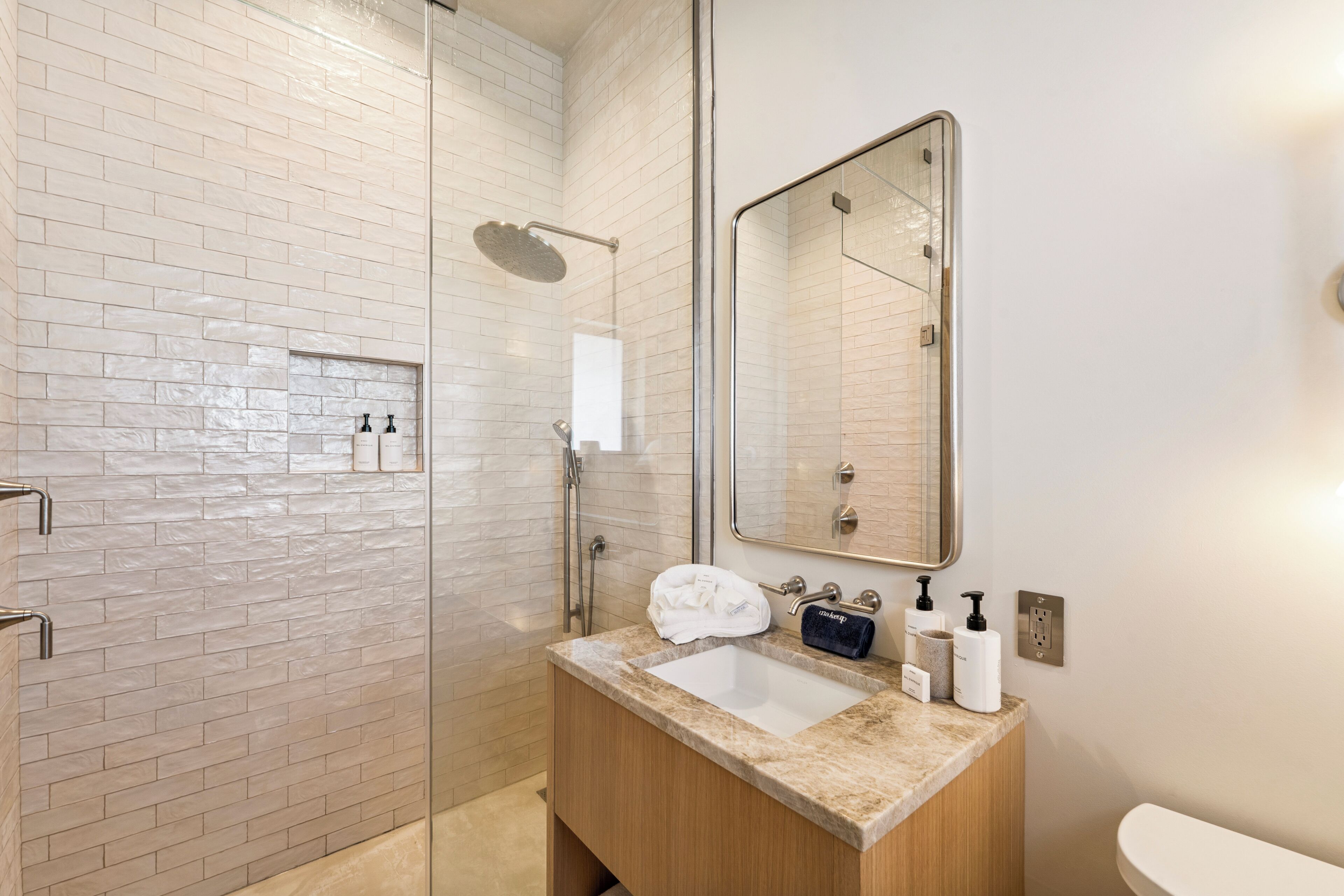 Une salle de bain moderne avec une douche à parois de verre, un lavabo doté d’un plan de travail en marbre et un grand miroir.