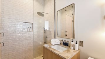 Une salle de bain moderne avec une douche à parois de verre, un lavabo doté d’un plan de travail en marbre et un grand miroir.