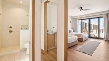 A modern hotel room with a shower, toilet, and a large bed with a view of the outdoors.