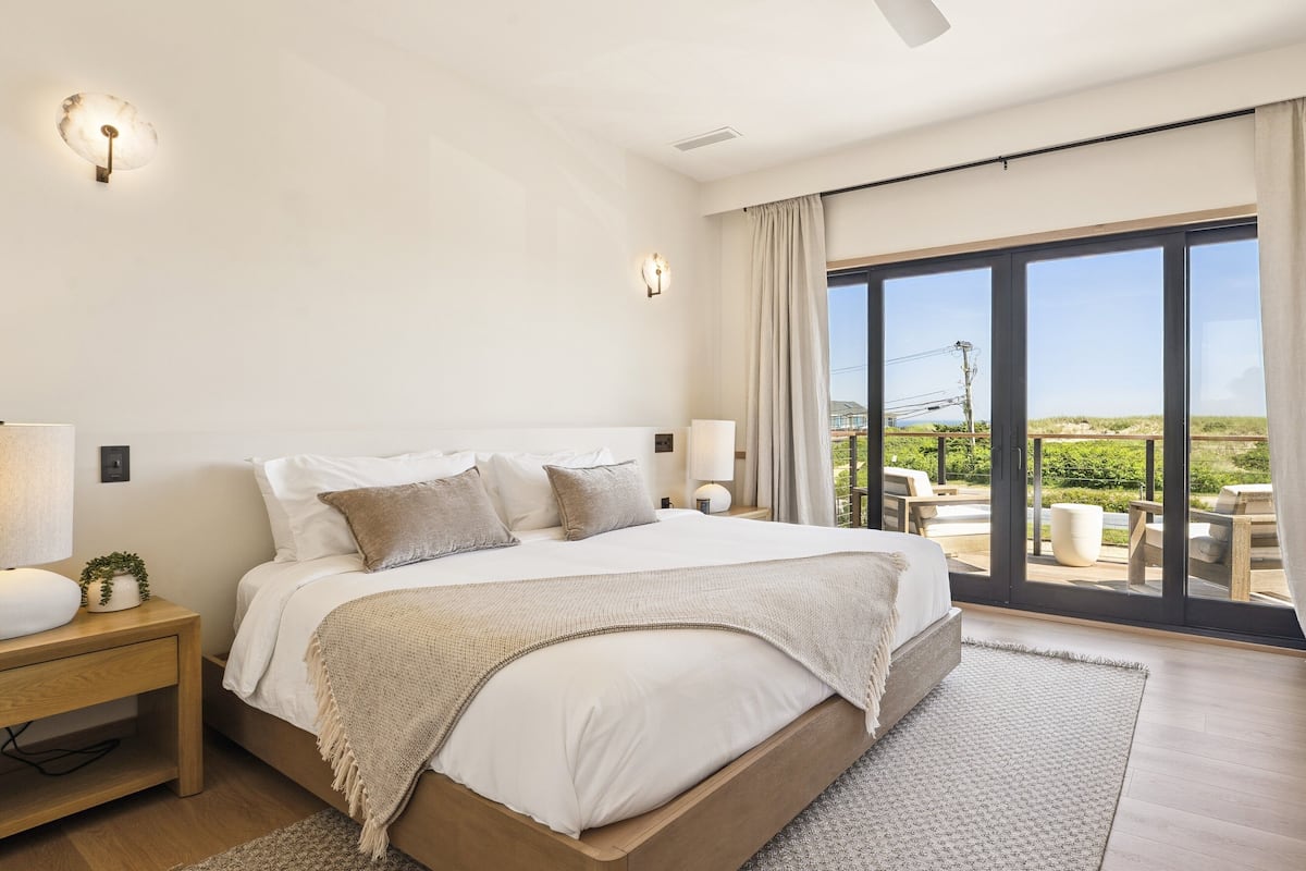 Une chambre dotée d’un grand lit, d’un ventilateur de plafond et offrant une vue sur l’extérieur grâce à une porte-fenêtre coulissante.