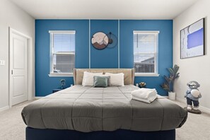A bedroom with a bed, two windows, a wall clock, and a small astronaut figurine.