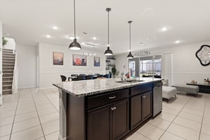 A modern kitchen with a central island, pendant lighting, and a dining area with chairs.