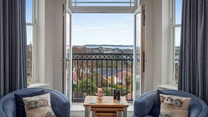 A room with a large window, two sofas, a small table with a bottle and glasses, and a view of a cityscape. - 10 Mansion House - Indoor Pool, Sea Views, Gym (Tenby)