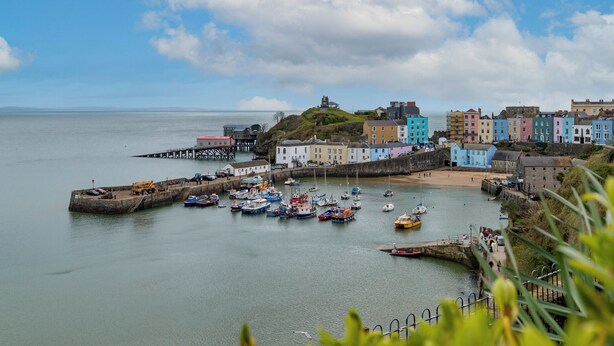 A coastal town with colorful buildings, a harbor with boats, and a lighthouse on a hill. - 10 Mansion House - Indoor Pool, Sea Views, Gym (Tenby)