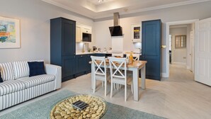 A modern kitchen with dark blue cabinets, a white dining table, and a striped sofa. - 10 Mansion House - Indoor Pool, Sea Views, Gym (Tenby)