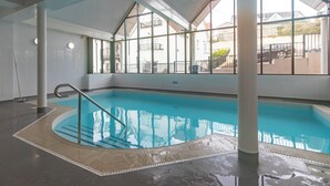 An indoor swimming pool with clear glass walls, a tiled floor, and a metal ladder. - 10 Mansion House - Indoor Pool, Sea Views, Gym (Tenby)