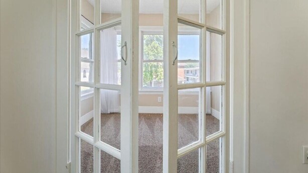 A room with a large window, carpeted floor, and white walls.