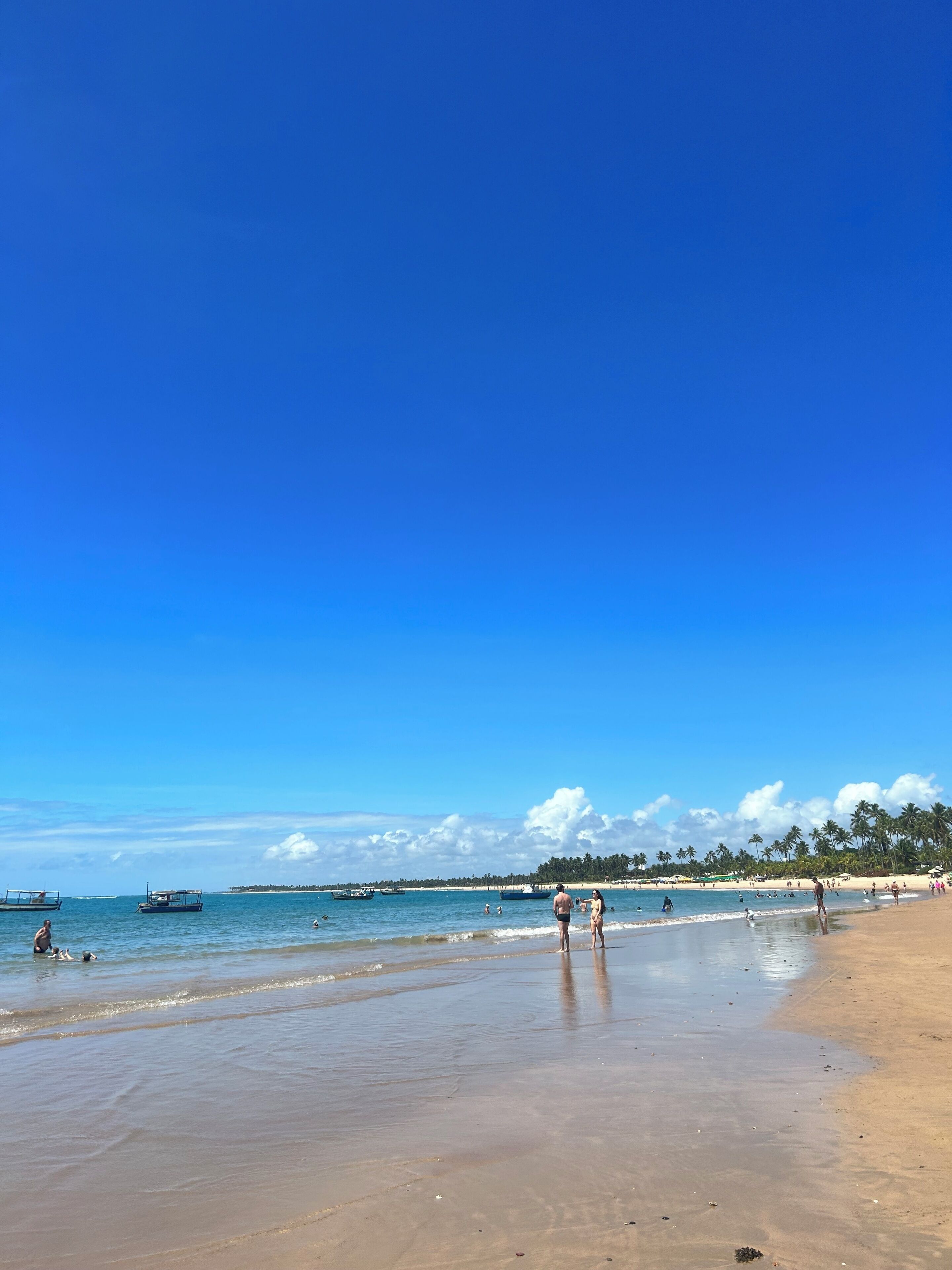 A beach with clear skies, calm water, and people enjoying the shore.