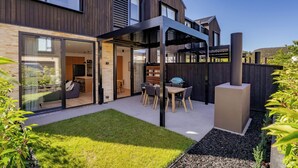A modern house with a patio, a dining area, and a large sliding glass door leading to a living space. - Explorers Rest - Wanaka Holiday Home (Wanaka)