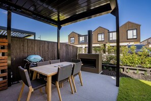Une terrasse couverte avec une table et des chaises en bois, un barbecue et une cheminée.