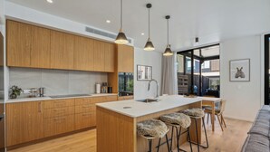 A modern kitchen with wooden cabinets, a central island, bar stools, and pendant lighting. - Explorers Rest - Wanaka Holiday Home (Wanaka)