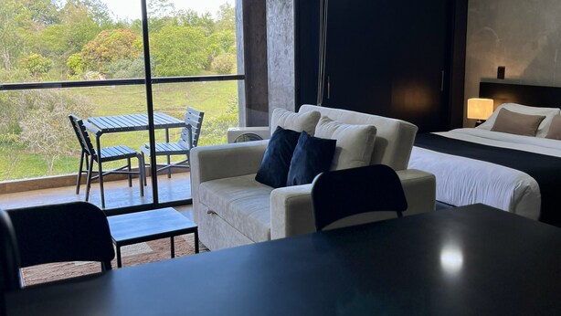 A modern hotel room with a large window, a sofa, a bed, and a small table. - Suites - Hotel Rioverde (Rionegro)