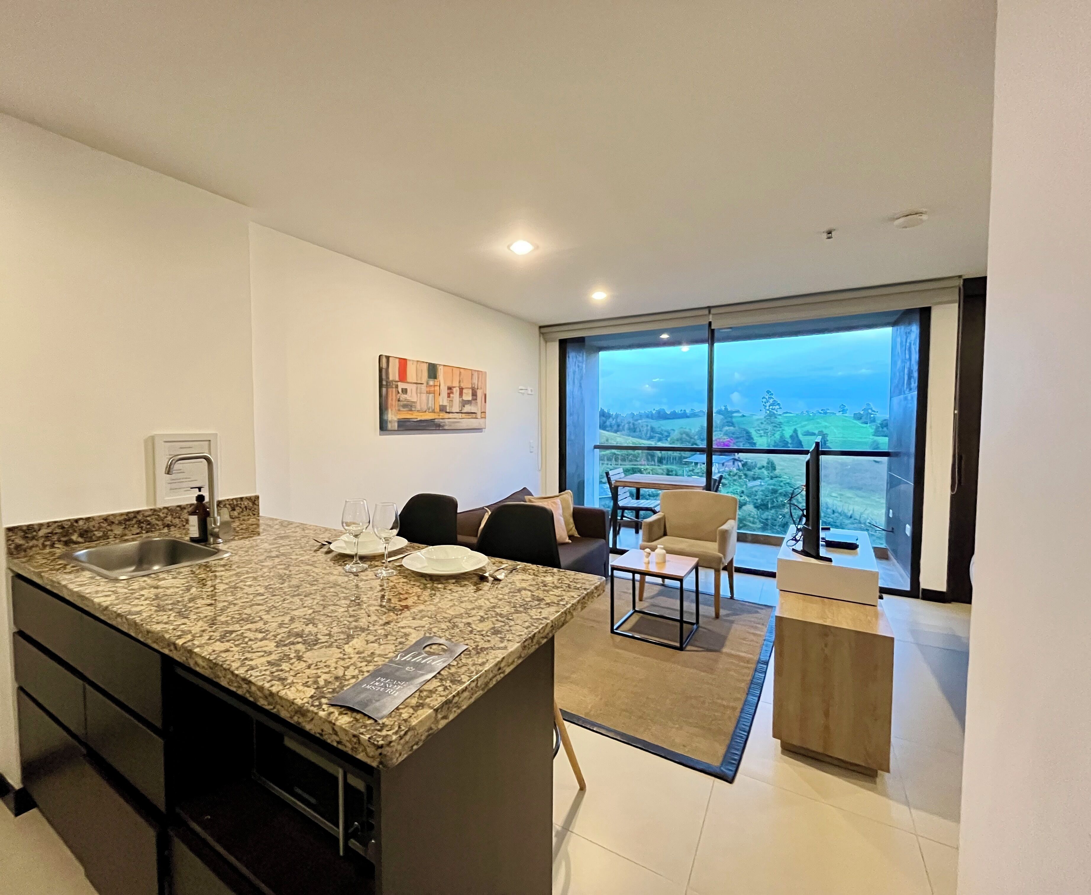A modern kitchen with granite countertops, a built-in sink, and a dining area with a view of the countryside.