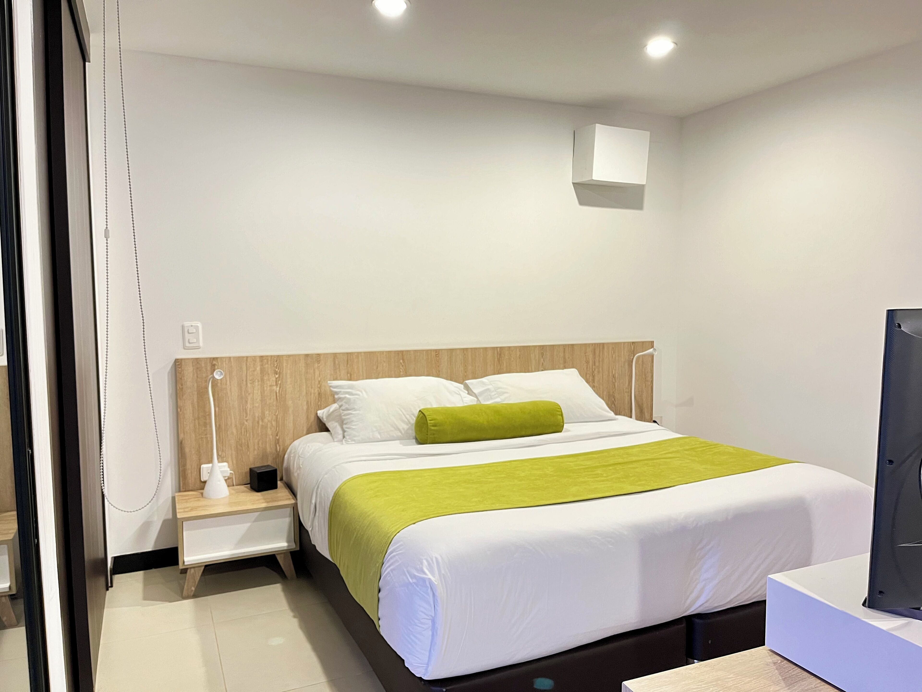 Une chambre d’hôtel équipée d’un lit, d’une table de chevet, d’une télévision et d’une lampe fixée au mur.