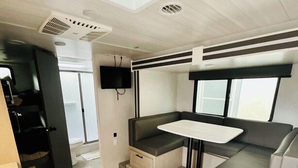 A compact RV interior with a kitchenette, a seating area with a table, and a television mounted on the wall.