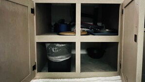 A kitchen with wooden cabinets, a built-in microwave, and a trash bin.