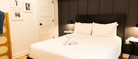 A neatly made bed with white linens and rolled towels, a wooden nightstand with a lamp, and a small round table with a phone.