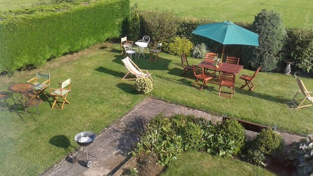 Un vaste espace extérieur comprenant une pelouse, des coins salon et un barbecue.