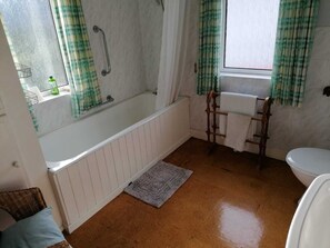 A bathroom with a bathtub, a toilet, and a window with curtains. - Montalto Farmhouse in the Glens of Antrim, Northern Ireland. (Newtown-Crommelin)
