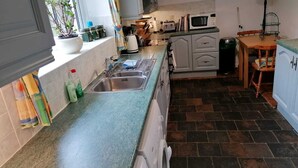 Une cuisine compacte équipée d’un évier, d’un four à micro-ondes et d’une cuisinière. On y trouve également des placards et une fenêtre agrémentée de plantes.