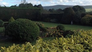 Un jardin aménagé avec des haies soigneusement taillées, une pelouse et des collines qui se dessinent à l’horizon.