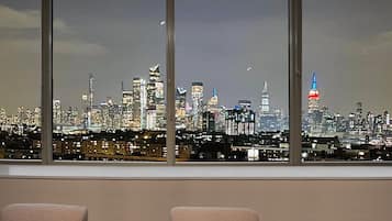 Uitzicht op een stadshemelbeeld door grote ramen, met meerdere hoge gebouwen en een opvallende toren met rode en blauwe verlichting.