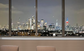 Vista del horizonte urbano a través de amplios ventanales, con varios rascacielos y una torre destacada con luces rojas y azules.