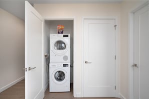 Un lavadero con dos lavadoras apiladas y una puerta a otra habitación.