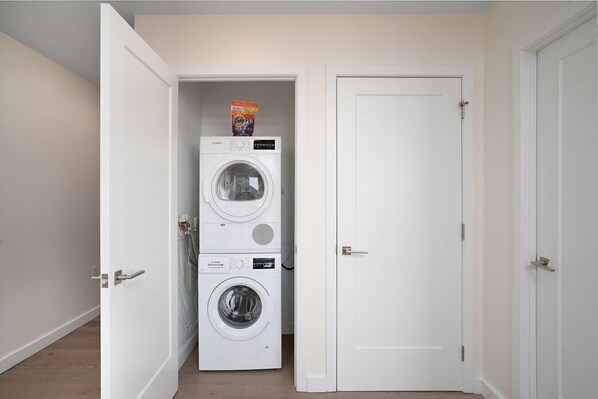Un lavadero con dos lavadoras apiladas y una puerta a otra habitación.