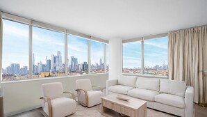 Ein modernes Wohnzimmer mit großem Fenster und Blick auf die Stadt, ein weißes Sofa, zwei Sessel und ein Holztisch.