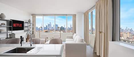 A modern living room with a city view, a kitchen area, and a flat-screen TV displaying 'NETFLIX'.