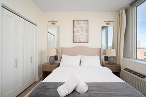 A hotel room with a large bed, two bedside tables with lamps, a large window with curtains, and a city view.