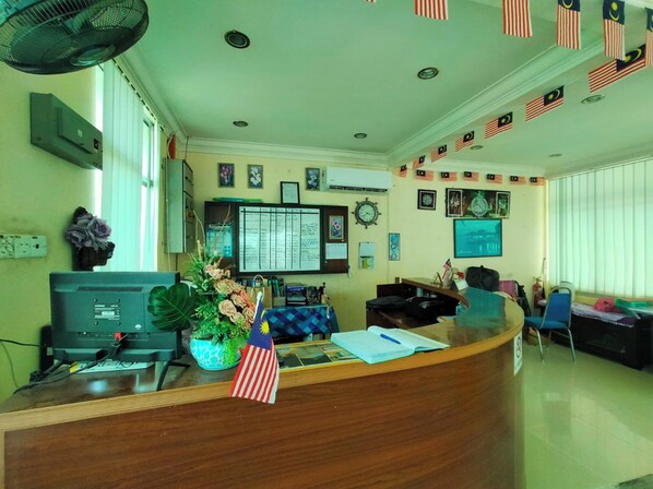 A reception area with a wooden desk, a computer, a plant, and flags on the wall.