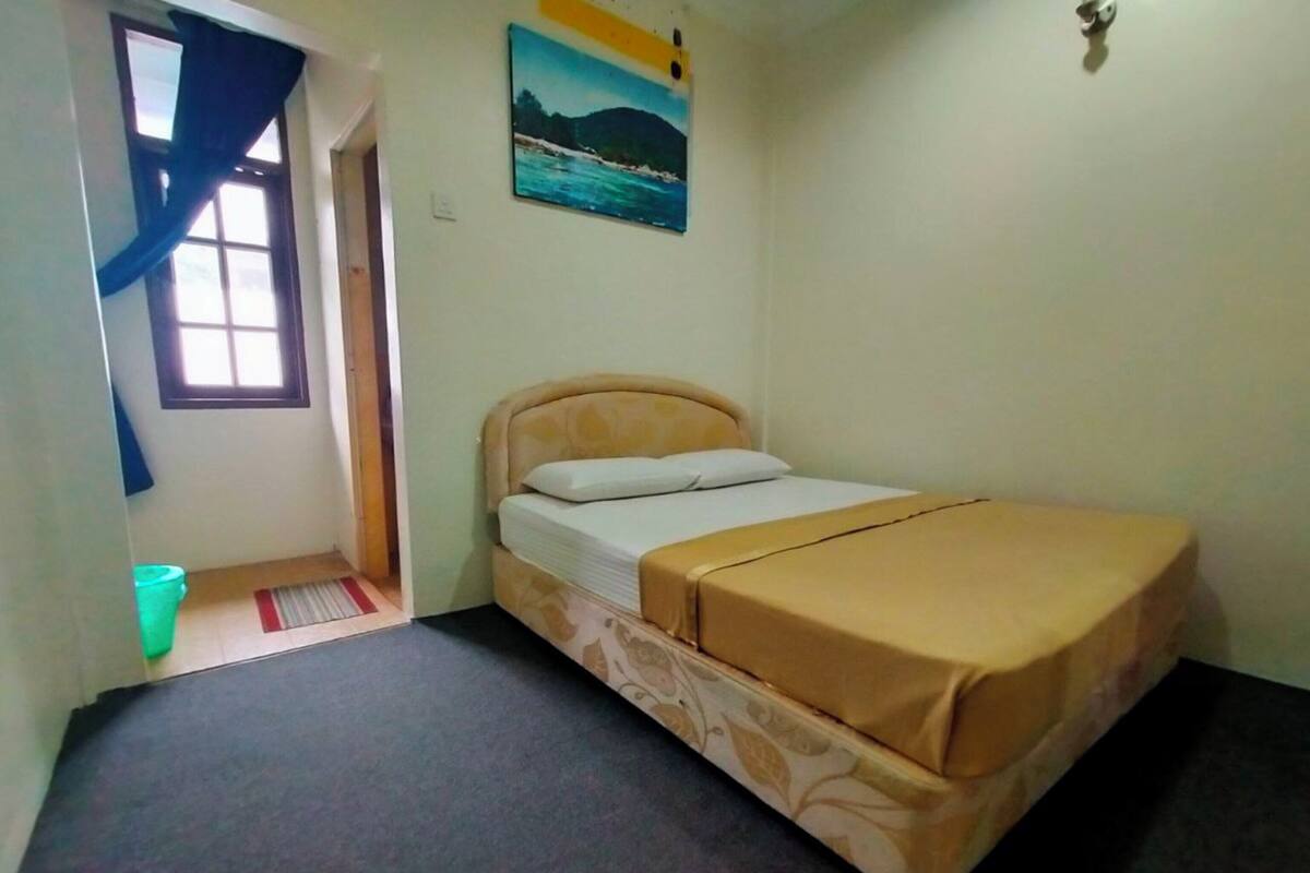 Ein kleines Zimmer mit einem Einzelbett, einer gestreiften Bettdecke, einem Bild an der Wand und einem Fenster mit Vorhängen.