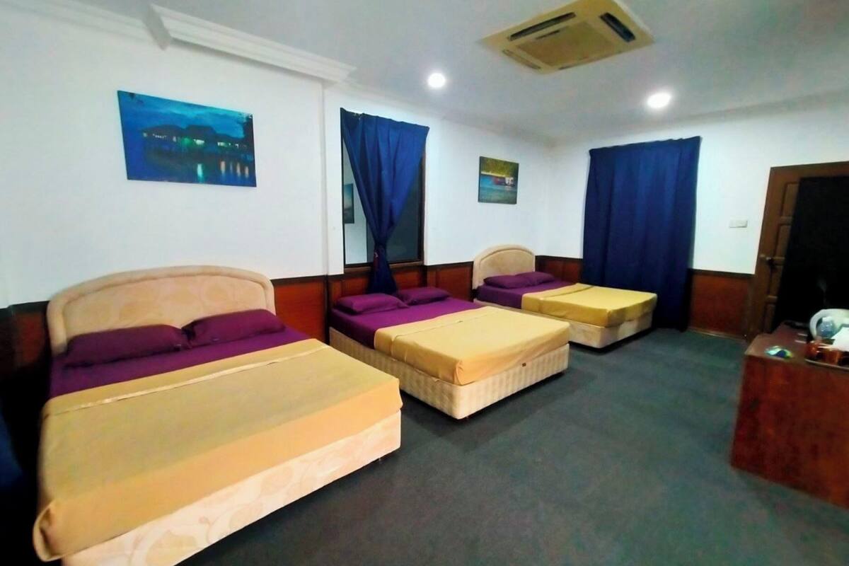 Ein Hotelzimmer mit drei Betten, einem Holz-Kopfteil, einem kleinen Schreibtisch und einem Wandbild mit Nachtansicht.