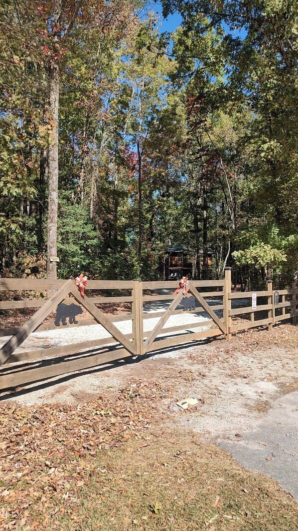 A wooden gate with a 'Private Drive' sign, leading to a forested area with a house in the background.