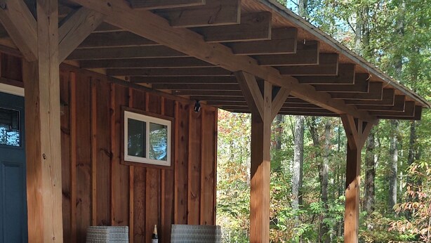 Eine Holzhütte mit überdachter Veranda, Korbmöbeln und Blumentöpfen.
