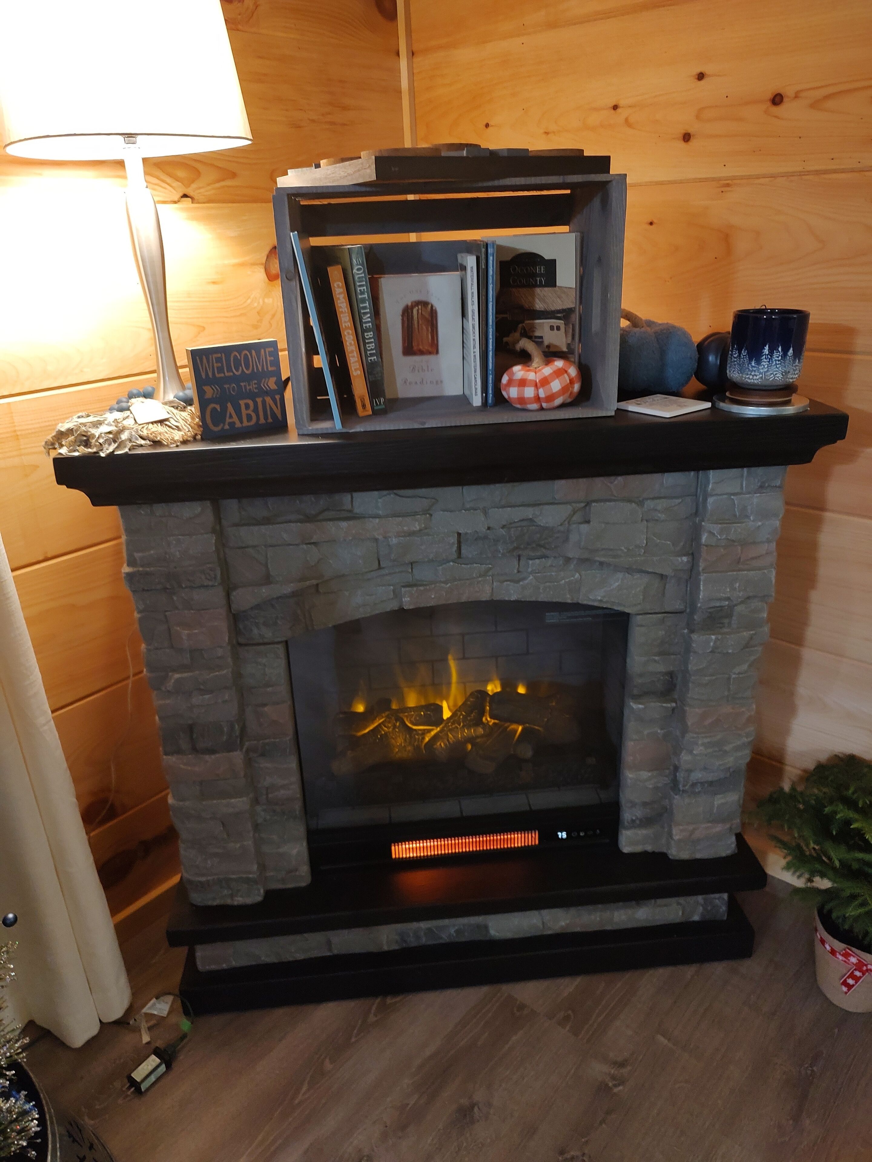 Een stenen open haard met een bovenkant waarop boeken, een welkomstbord en decoratieve objecten staan.