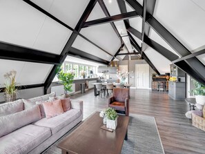 A spacious loft with a high ceiling, exposed beams, a kitchen area, and a seating area with a sofa and armchair. - Luxury Wellness apartment with view (Reutum)